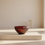 Decorative red and black bowl with intricate designs on a gray background